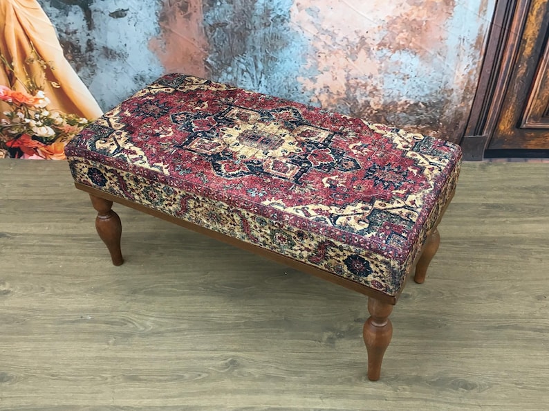 Puede incluir: Un banco de madera rectangular con patas torneadas. El asiento est&aacute; tapizado con una tela estampada de colores que recuerda a una alfombra tradicional.
