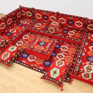 Peut inclure: Un canapé modulaire rouge avec un motif géométrique de différentes couleurs. L'ensemble comprend un canapé d'angle, un ottoman rectangulaire et plusieurs coussins. Le design présente un style traditionnel et ethnique.