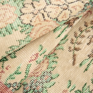 May include: Close-up of a beige rug with a floral pattern. The rug has a woven texture and features green, brown, and pink floral designs.