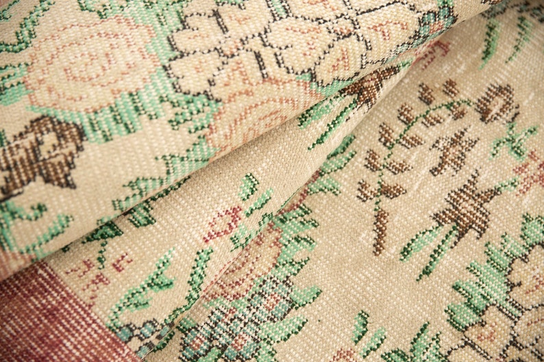 May include: Close-up of a beige rug with a floral pattern. The rug has a woven texture and features green, brown, and pink floral designs.