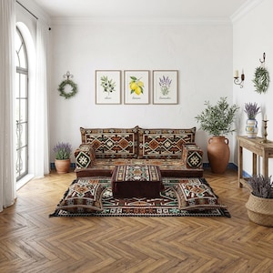 May include: A living room scene featuring a low-profile sofa and matching ottoman set with a geometric pattern in shades of brown, green, and red. The room includes framed botanical prints, a large terracotta vase, and a wooden side table.
