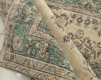 Könnte beinhalten: Ein Vintage-Teppich mit cremefarbenem Hintergrund und grünem Blumenmuster. Der Teppich ist in der Mitte gefaltet und zeigt die Rückseite.