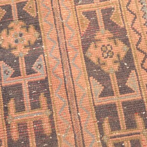 May include: A vintage rug with a geometric pattern in shades of pink, brown, and gray. The rug has a fringed edge and is woven with a traditional design.