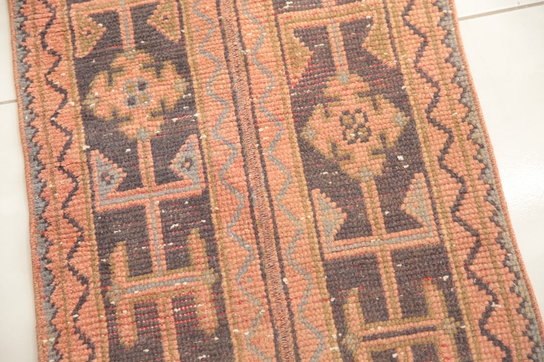 May include: A vintage rug with a geometric pattern in shades of pink, brown, and gray. The rug has a fringed edge and is woven with a traditional design.
