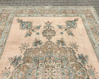 Op de afbeelding: Een groot rechthoekig vloerkleed met een zachte perzikkleurige achtergrond, voorzien van een complex centraal medaillon en bloemmotieven in tinten blauwgroen, saliegroen en bruin. Het kleed heeft een brede decoratieve rand met herhalende patronen.