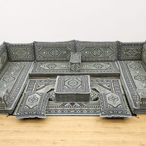 Könnte beinhalten: Ein graues und weiß gemustertes Sitzset für den Boden mit einem zentralen quadratischen Ottoman. Das Set enthält mehrere Kissen und einen großen rechteckigen Teppich.