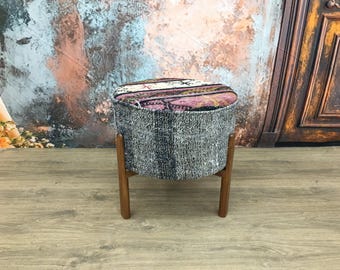 May include: A round, gray and pink patterned ottoman with wooden legs. The ottoman is sitting on a wooden floor.