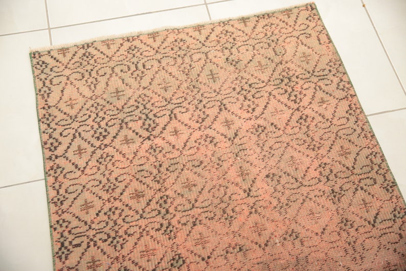 May include: A pink and black patterned rug with a geometric design. The rug has a distressed look and is made of a woven material.
