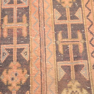 May include: A vintage runner rug with a geometric pattern in shades of pink, brown, and gray. The rug has a fringed edge.