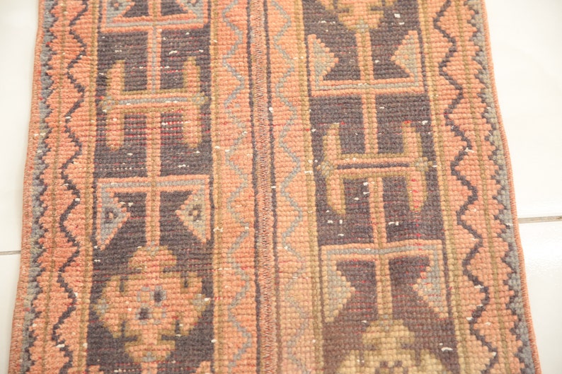 May include: A vintage runner rug with a geometric pattern in shades of pink, brown, and gray. The rug has a fringed edge.