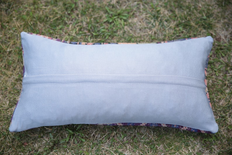 Puede incluir: Una almohada rectangular de color gris claro con cierre de cremallera. La almohada est&aacute; hecha de una tela suave y lisa con un brillo sutil. La almohada est&aacute; tumbada sobre un lecho de hierba verde.