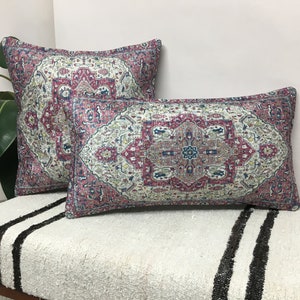 May include: Two decorative throw pillows with a pink, blue, and white patterned design. The pillows are on a white and black striped surface.