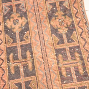 May include: A vintage runner rug with a geometric pattern in shades of pink, brown, and gray. The rug has a fringed edge and is made of wool.