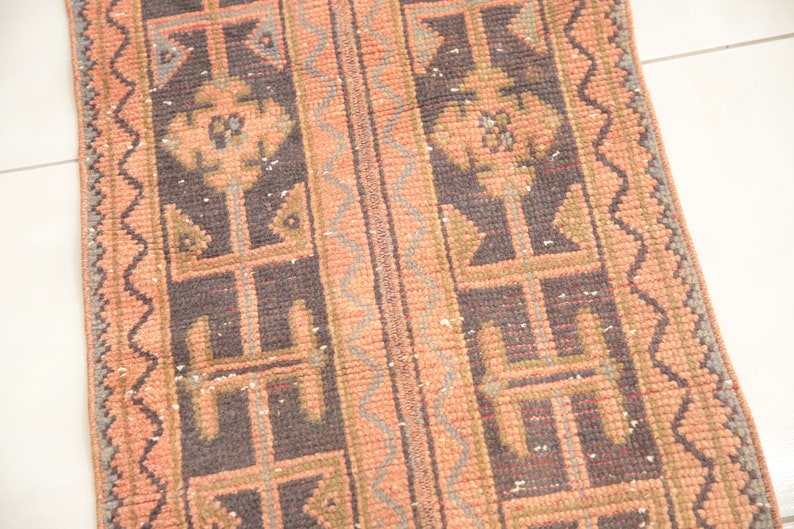 May include: A vintage runner rug with a geometric pattern in shades of pink, brown, and gray. The rug has a fringed edge and is made of wool.