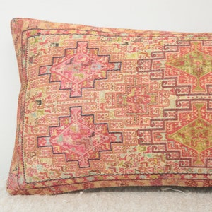 May include: A long, rectangular pillow with a pink, red, and cream patterned fabric. The pattern is a geometric design with intricate details.