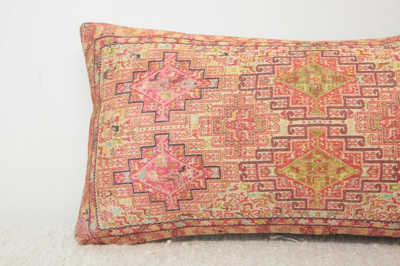 May include: A long, rectangular pillow with a pink, red, and cream patterned fabric. The pattern is a geometric design with intricate details.