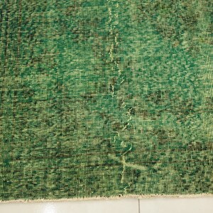K&ouml;nnte beinhalten: Ein gr&uuml;ner Vintage-Teppich mit einem abgenutzten Look. Der Teppich hat ein dezentes Muster und einen Fransenrand.