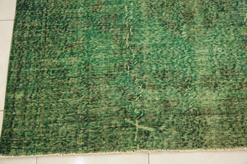 K&ouml;nnte beinhalten: Ein gr&uuml;ner Vintage-Teppich mit einem abgenutzten Look. Der Teppich hat ein dezentes Muster und einen Fransenrand.