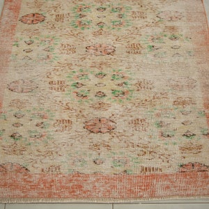 May include: A vintage rug with a floral pattern in shades of pink, green, and brown. The rug has a peach-colored border and a fringed edge.