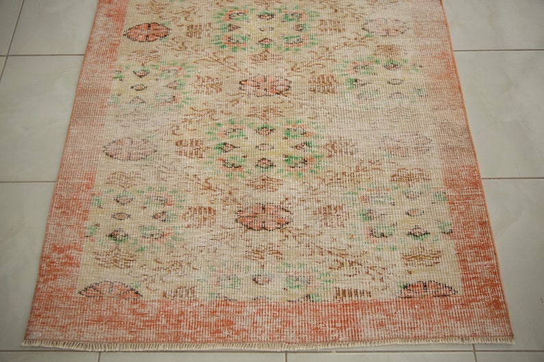 May include: A vintage rug with a floral pattern in shades of pink, green, and brown. The rug has a peach-colored border and a fringed edge.