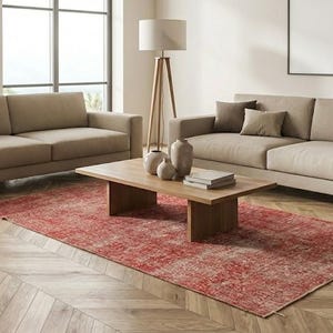 Può includere: Due divani in tessuto beige con cuscini decorativi marrone scuro, un tavolino rettangolare in legno con tre vasi in ceramica e una pila di libri, e un grande tappeto rettangolare rosso a motivi su un pavimento in legno a spina di pesce.