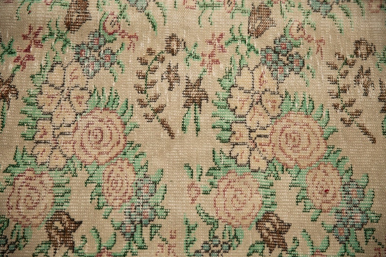 May include: Close-up of a beige rug with a floral pattern. The rug features a repeating design of pink and white roses with green leaves.