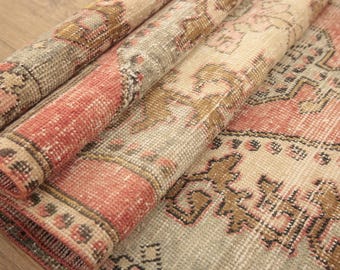 Può includere: Un tappeto intrecciato con un motivo sbiadito nei toni del corallo, beige e marrone. Il tappeto è ripiegato, rivelando una superficie a pelo testurizzato con intricati motivi geometrici e floreali su tutto il tessuto in un design ripetuto.