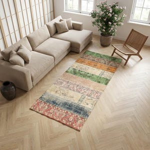 May include: A rectangular, multi-coloured rug with a patchwork design. The rug features various rectangular sections in shades of red, blue, green, orange, and beige. The rug is placed on a light-coloured wooden floor, near a beige sectional sofa.