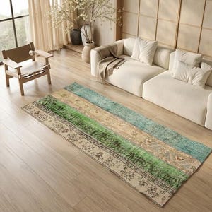 May include: A rectangular area rug with a patchwork design. The rug features sections of green, beige, and blue, with floral and geometric patterns. The rug is placed on a wooden floor in a living room setting.