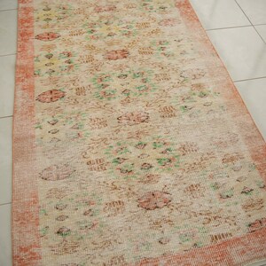 May include: A vintage style rug with a floral pattern in shades of pink, green, and white. The rug has a distressed look with faded colors and a worn texture.