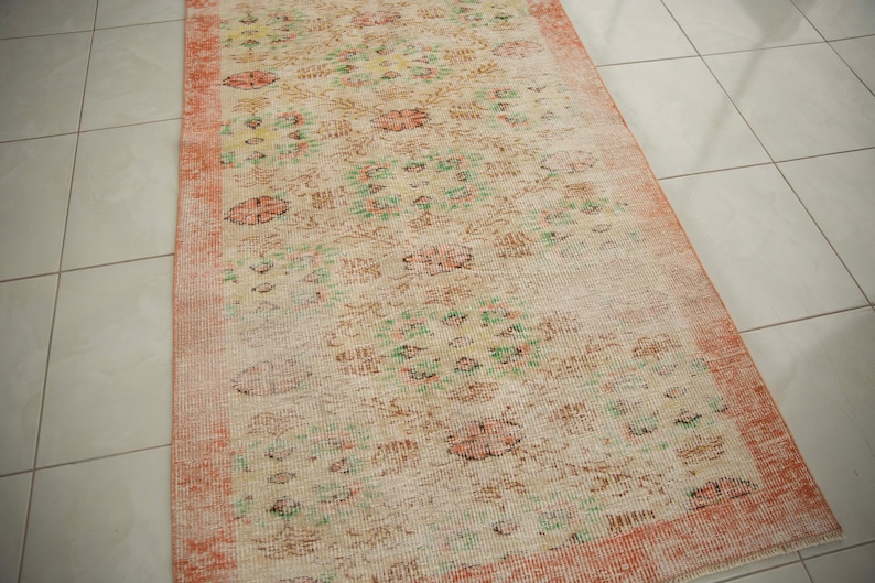 May include: A vintage style rug with a floral pattern in shades of pink, green, and white. The rug has a distressed look with faded colors and a worn texture.
