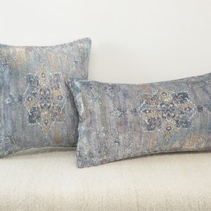 May include: Two decorative throw pillows with a blue and beige patterned design. The pillows have a geometric pattern with a floral motif.