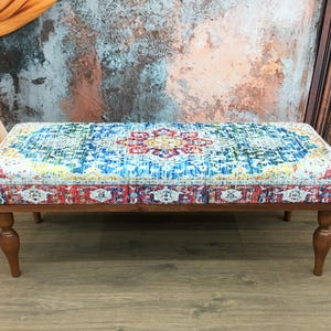 May include: A colorful patterned bench with a wooden frame and turned legs. The bench has a bright blue, red, yellow, and green patterned fabric top.
