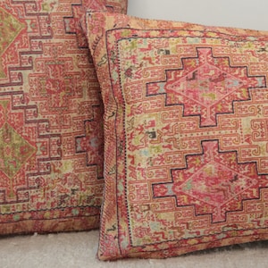 May include: Two decorative throw pillows with a red, pink, and cream patterned design. The pattern features intricate geometric shapes and a diamond-shaped center.