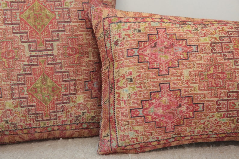 May include: Two decorative throw pillows with a red, pink, and cream patterned design. The pattern features intricate geometric shapes and a diamond-shaped center.