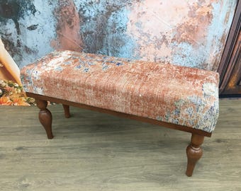 Puede incluir: Banco rectangular con una parte superior estampada y desgastada en tonos naranja, azul y blanco. El banco tiene un marco de madera oscura y cuatro patas torneadas. El banco es una pieza de mobiliario decorativa.