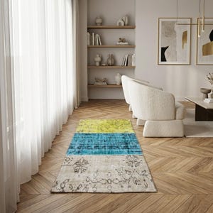 May include: A rectangular rug with a colour block design. The rug features a yellow, blue, and beige colour scheme. The beige section has a floral pattern. The rug is placed on a wooden floor in a living room setting.