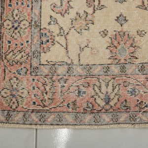 May include: A close-up of the bottom edge of a beige rug with a floral pattern. The rug has a fringe border and a detailed design with pink, blue, and brown accents.