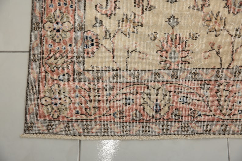 May include: A close-up of the bottom edge of a beige rug with a floral pattern. The rug has a fringe border and a detailed design with pink, blue, and brown accents.