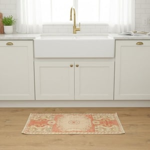 May include: A rectangular area rug featuring a central medallion design in shades of coral, cream, and sage green. The rug has a distressed, vintage-inspired pattern with a decorative border, positioned on a light brown wood-look floor in a kitchen.
