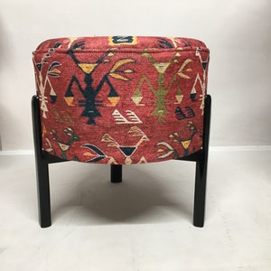 Puede incluir: Un puf redondo de color rojo y negro con estampado y un marco de madera negro. El puf tiene un dise&ntilde;o geom&eacute;trico con colores rojo, amarillo, azul y verde.