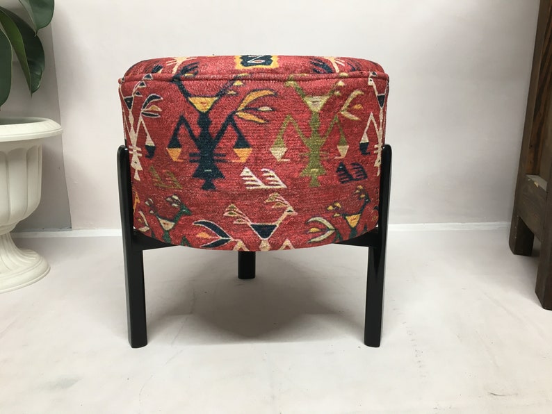 Puede incluir: Un puf redondo de color rojo y negro con estampado y un marco de madera negro. El puf tiene un dise&ntilde;o geom&eacute;trico con colores rojo, amarillo, azul y verde.