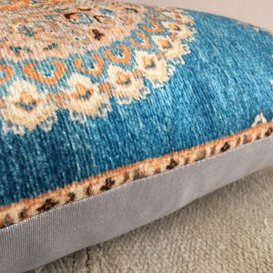 May include: A teal blue throw pillow with a multi-colored geometric pattern. The pillow has a light gray fabric backing.