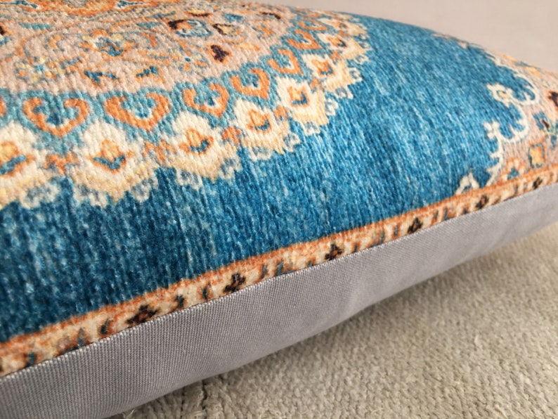 May include: A teal blue throw pillow with a multi-colored geometric pattern. The pillow has a light gray fabric backing.