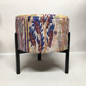 May include: A round ottoman with a colorful floral pattern fabric cover and black wooden legs.