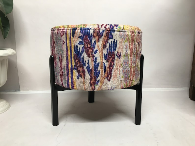 May include: A round ottoman with a colorful floral pattern fabric cover and black wooden legs.