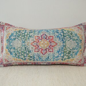 May include: A rectangular pillow with a colorful, intricate pattern. The pattern features a central floral design with shades of red, yellow, blue, and green.