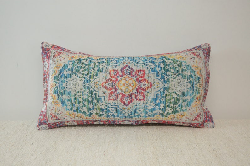 May include: A rectangular pillow with a colorful, intricate pattern. The pattern features a central floral design with shades of red, yellow, blue, and green.