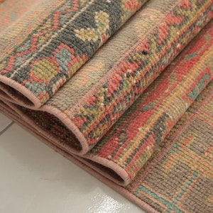 May include: A folded rug with a pink, red, green, and blue geometric pattern. The rug has a fringe on one end.