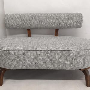 May include: A small loveseat featuring a rounded, oval-shaped seat upholstered in a textured grey and white woven fabric. It has a low, rectangular backrest supported by two wooden posts and stands on four curved, dark brown wooden legs.